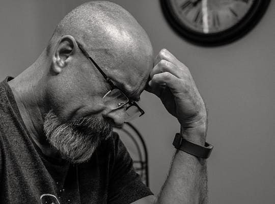 grayscale photo of man thinking in front of analog wall clock